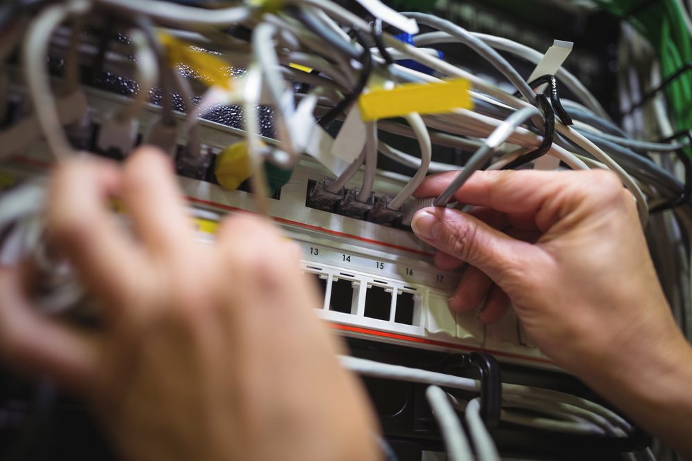Hands plugging labelled patch cables into a network patch panel